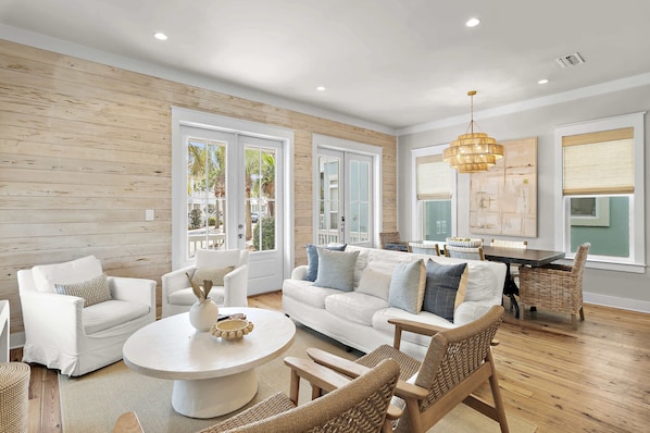 A spacious living room with a white sofa, two white armchairs, a round coffee table, and wicker chairs.