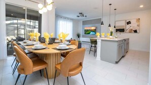 A modern kitchen with a dining area, featuring a round wooden table, brown chairs, and a central island with a sink. - Cozy 4Bd w Private Pool at Storey Lake Resort 2653 (Kissimmee)