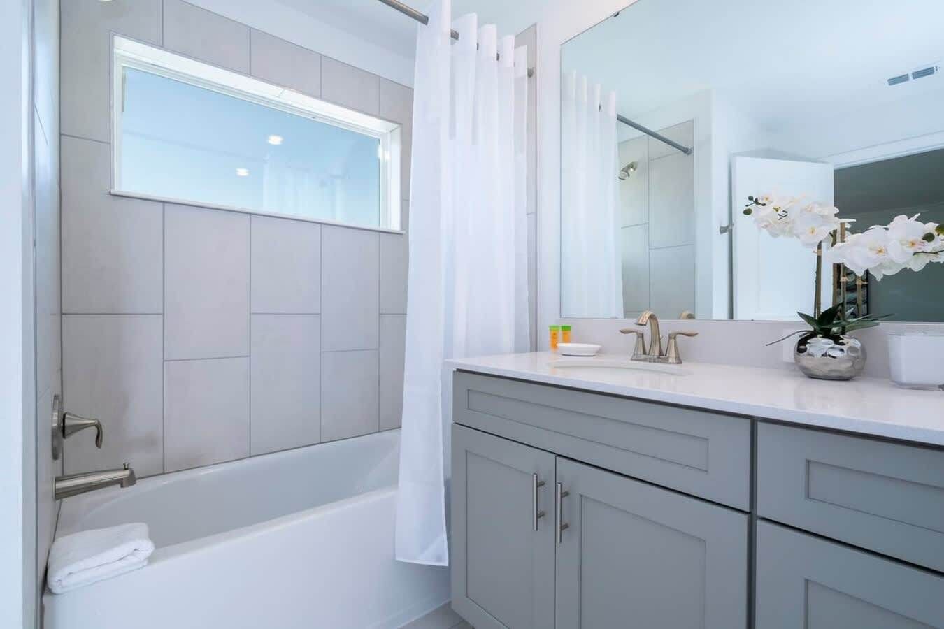 A modern bathroom with a bathtub, a vanity with a mirror, and a potted orchid.