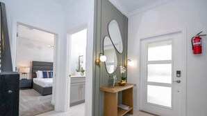 A modern hotel room with a large bed, a vanity with a mirror, and a door with a fire extinguisher. - Cozy 4Bd w Private Pool at Storey Lake Resort 2653 (Kissimmee)