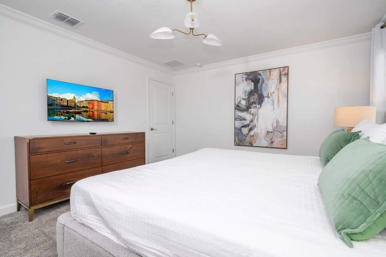 Une chambre à coucher avec un lit, une commode, un tableau et un luminaire au plafond.
