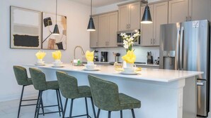 A modern kitchen with a central island, bar stools, pendant lighting, and stainless steel appliances. - Cozy 4Bd w Private Pool at Storey Lake Resort 2653 (Kissimmee)