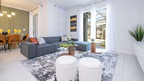 A modern living room with a grey sectional sofa, a round coffee table, and a dining area with a table and chairs. - Cozy 4Bd w Private Pool at Storey Lake Resort 2653 (Kissimmee)
