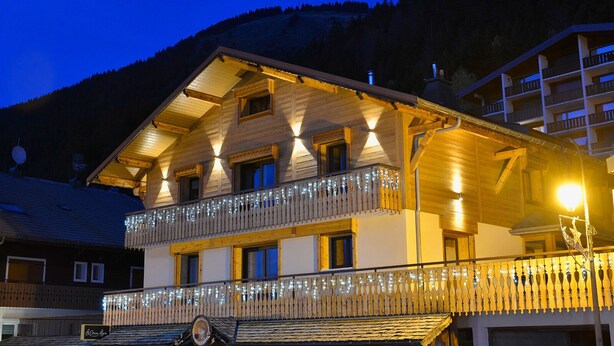 A multi-story wooden building with balconies, string lights, and a mountain backdrop. - Apartment for 8 people in the center of Châtel - Chatel Reservation (Châtel)