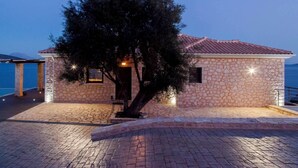 A stone building with a tiled roof, a tree in front, and a paved area.