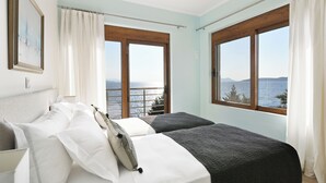 A bedroom with two beds, a view of the sea, and a balcony.