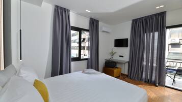 Una habitación de hotel moderna con una cama grande, un escritorio y un balcón con mesa y sillas.