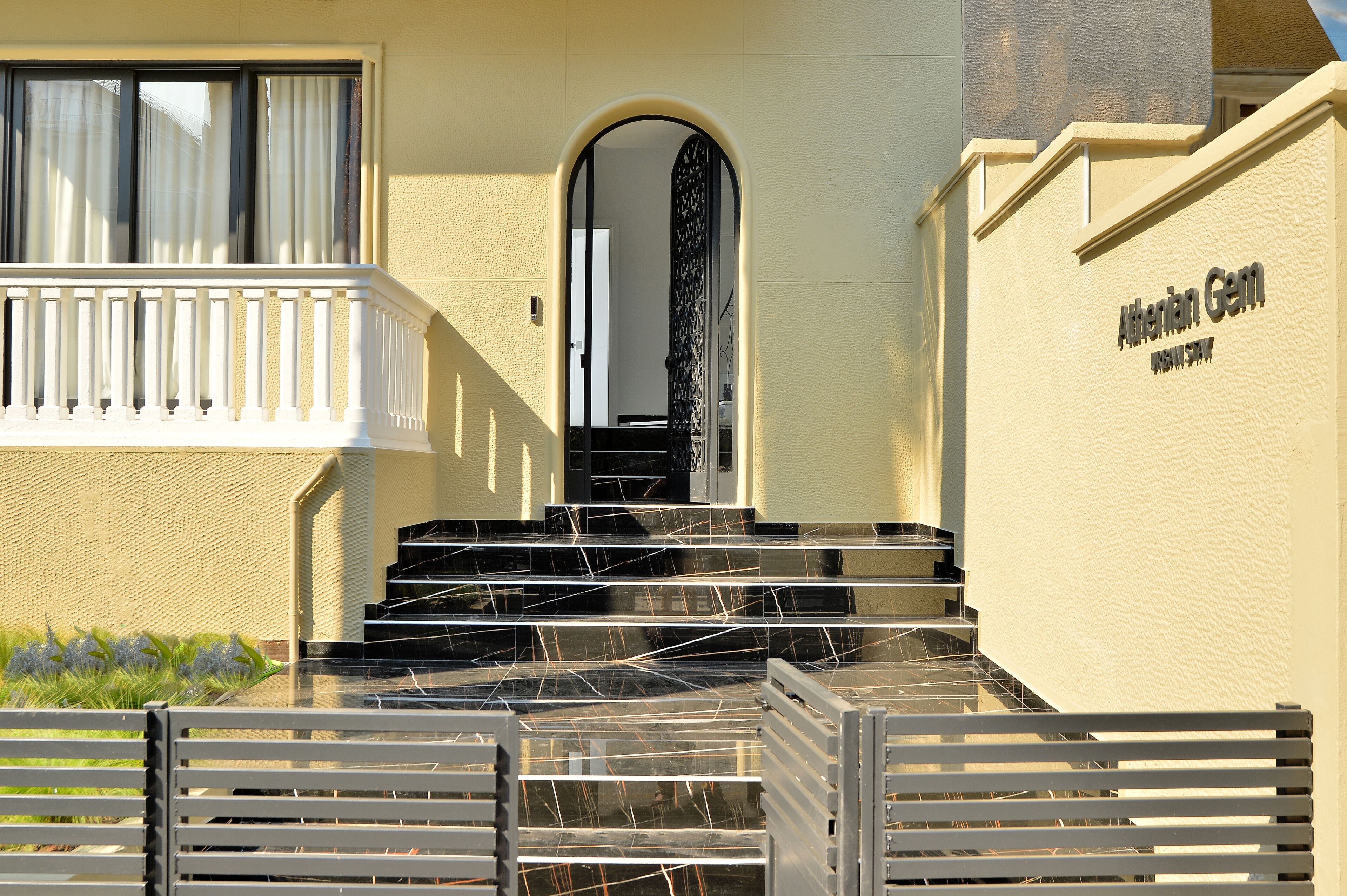 A hotel entrance with a marble staircase, a balcony with white railings, and a sign reading "Albanian Gem."