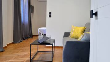 A modern living room with a grey sofa, a black coffee table, and a small table with a laptop and glasses.
