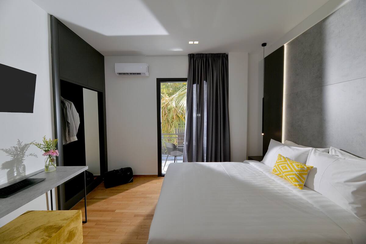 Una habitación de hotel moderna con una cama grande, un escritorio con una computadora portátil, una silla y vistas al exterior a través de una puerta corredera.