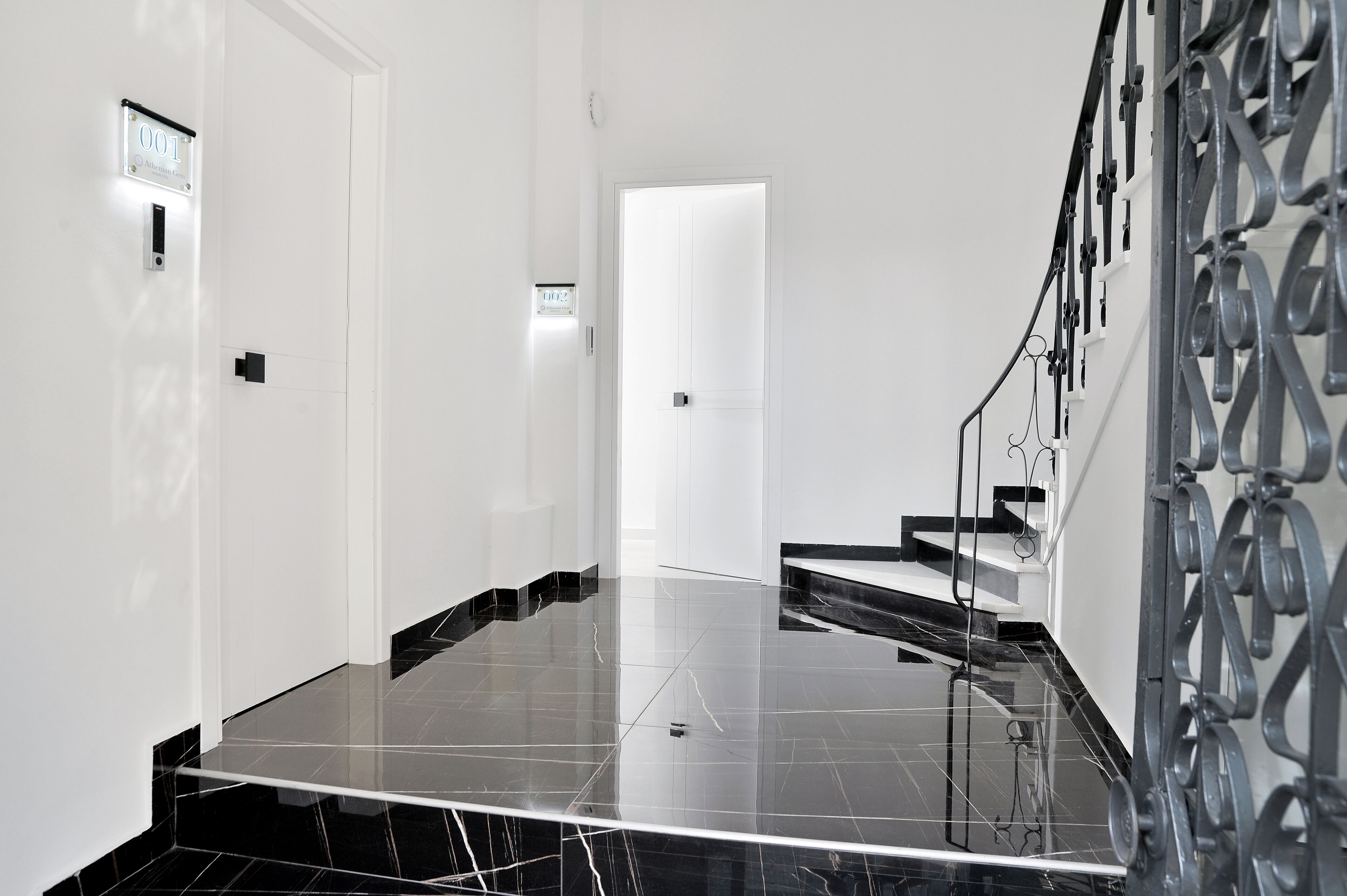 Un interior moderno con suelo de mármol negro, una puerta blanca y una escalera de metal con diseños elaborados.