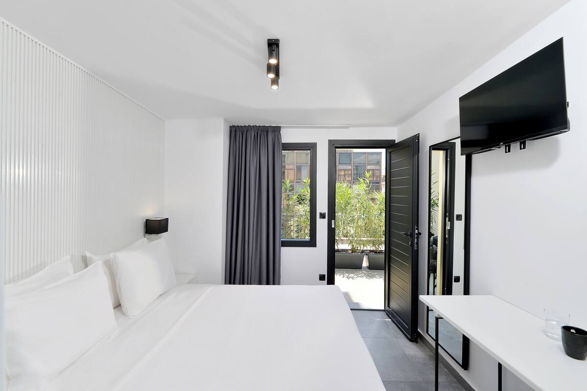 Un dormitorio moderno con una cama grande, un televisor de pantalla plana montado en la pared y un ventanal corredero que da a un espacio exterior.