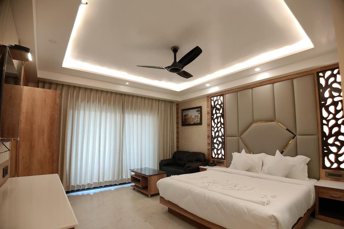 A modern hotel room with a large bed, a ceiling fan, a desk, and a view of the cityscape through the window.