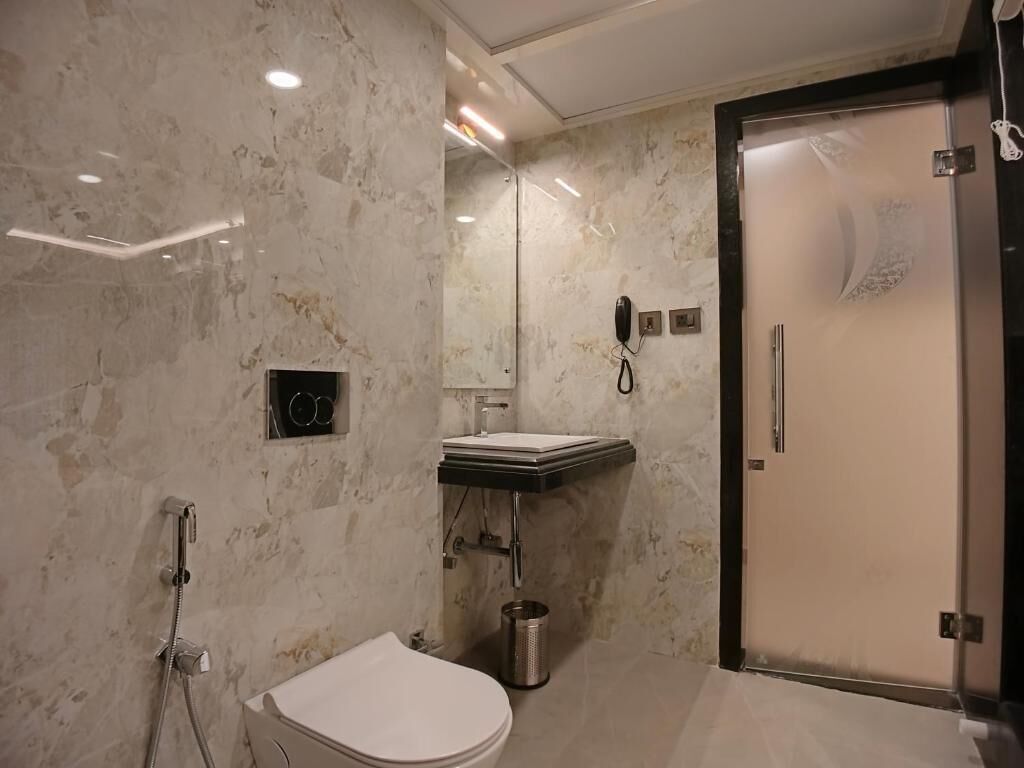 A modern bathroom with a marble wall, a toilet, a sink, and a shower.