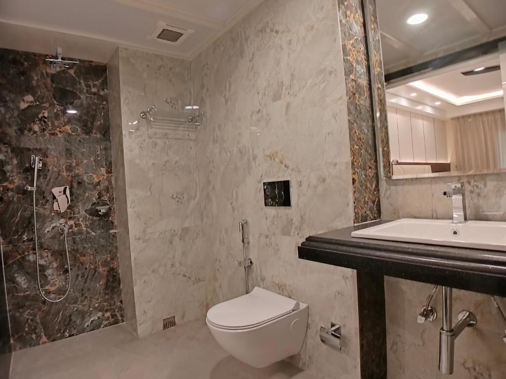 A modern bathroom with a marble shower, a toilet, and a sink with a dark countertop.