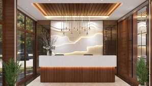 A reception area with a modern design, featuring a wooden reception desk, a large wall with a wave-like pattern, and hanging pendant lights. - AGM GRAND HOTEL & SPA (Kanthi)