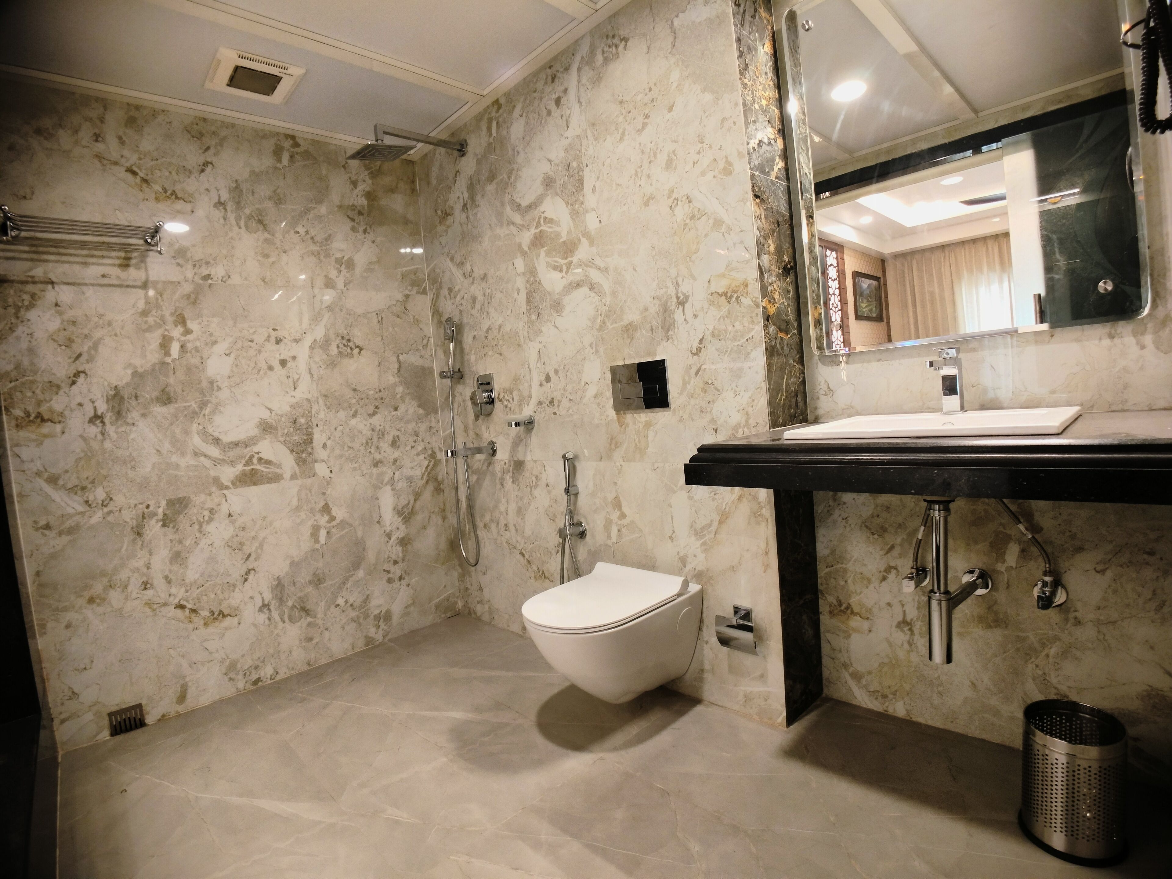 A modern bathroom with a marble floor, a white toilet, a black sink, and a shower with a handheld showerhead.