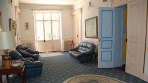 A room with two leather armchairs, a small table with a lamp, a patterned carpet, and a large window with a view of greenery. - Chateâu de Faudade (Levignac)
