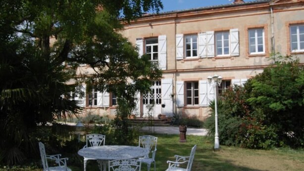 A two-story building with a garden patio featuring white metal chairs and a table. - Chateâu de Faudade (Levignac)