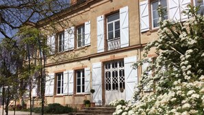 A two-story building with white shutters, a balcony, and a garden with white flowers. - Chateâu de Faudade (Levignac)