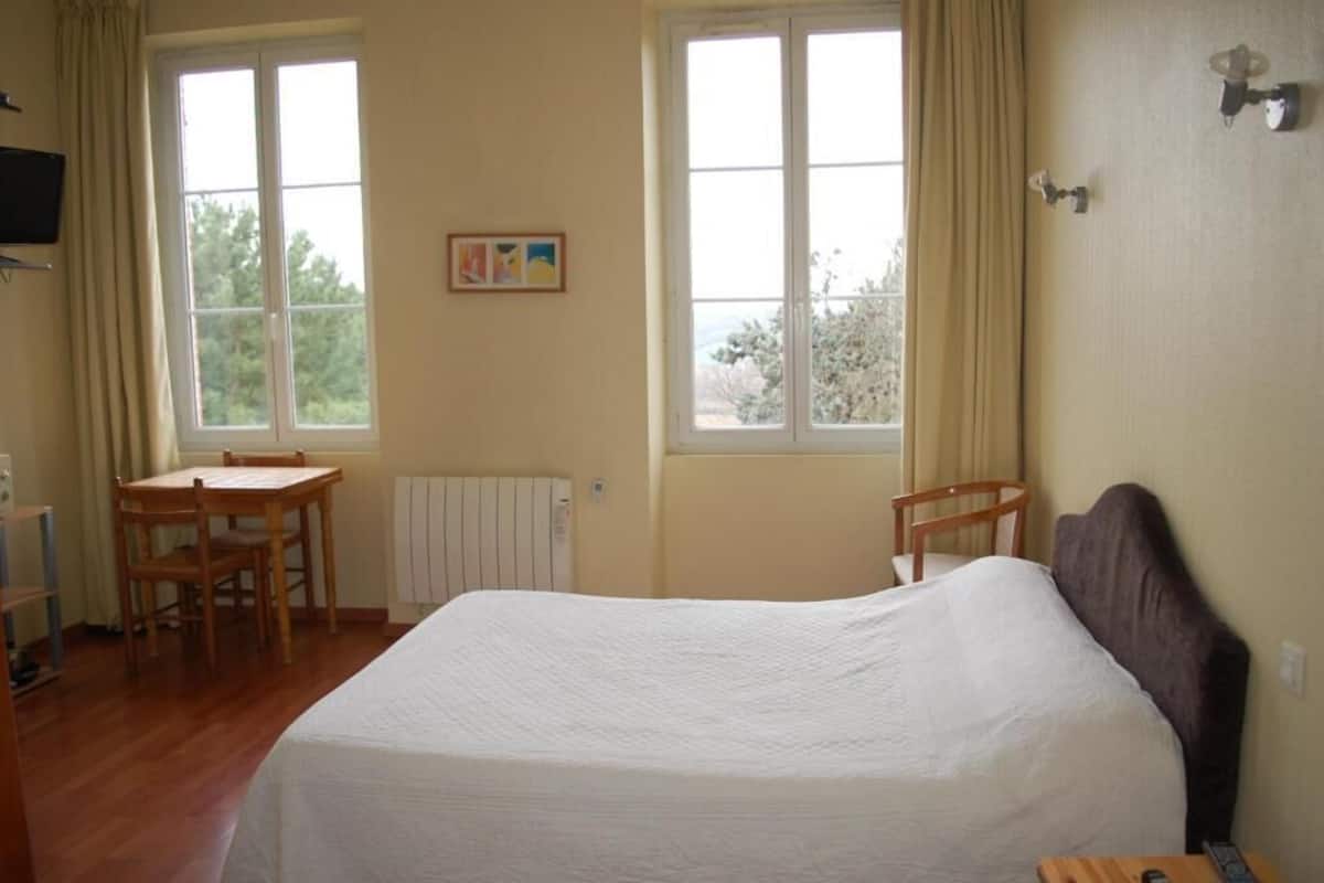 A bedroom with a bed, a desk, two chairs, and a radiator.