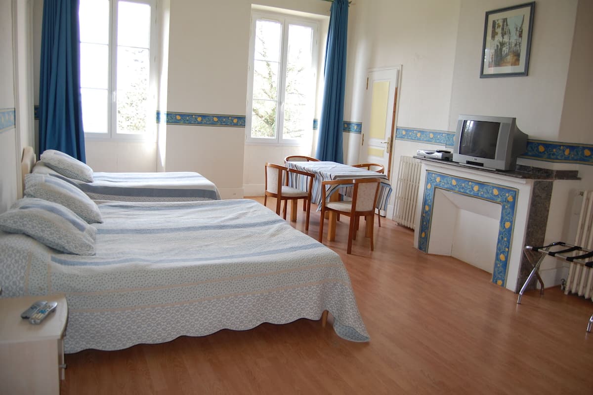 A hotel room with two beds, a dining table, chairs, a TV, and a radiator.