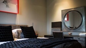 A hotel room with a bed, a desk, a chair, a dresser, a mirror, and a framed picture on the wall.