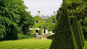 A large, ivy-covered building with a well-manicured lawn and neatly trimmed hedges.