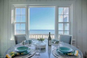 A dining table set for four with a view of the ocean through large windows. - Stunning Waterfront Views, Beach steps away! (Wellfleet)