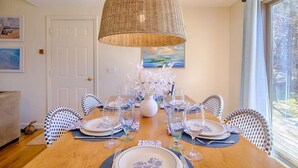 Une salle à manger avec une table en bois dressée pour six personnes, entourée de chaises à motifs, d’un luminaire décoratif suspendu et d’œuvres d’art encadrées accrochées aux murs.
