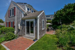 A two-story house with a covered porch, a small garden, and a visible outdoor grill area.