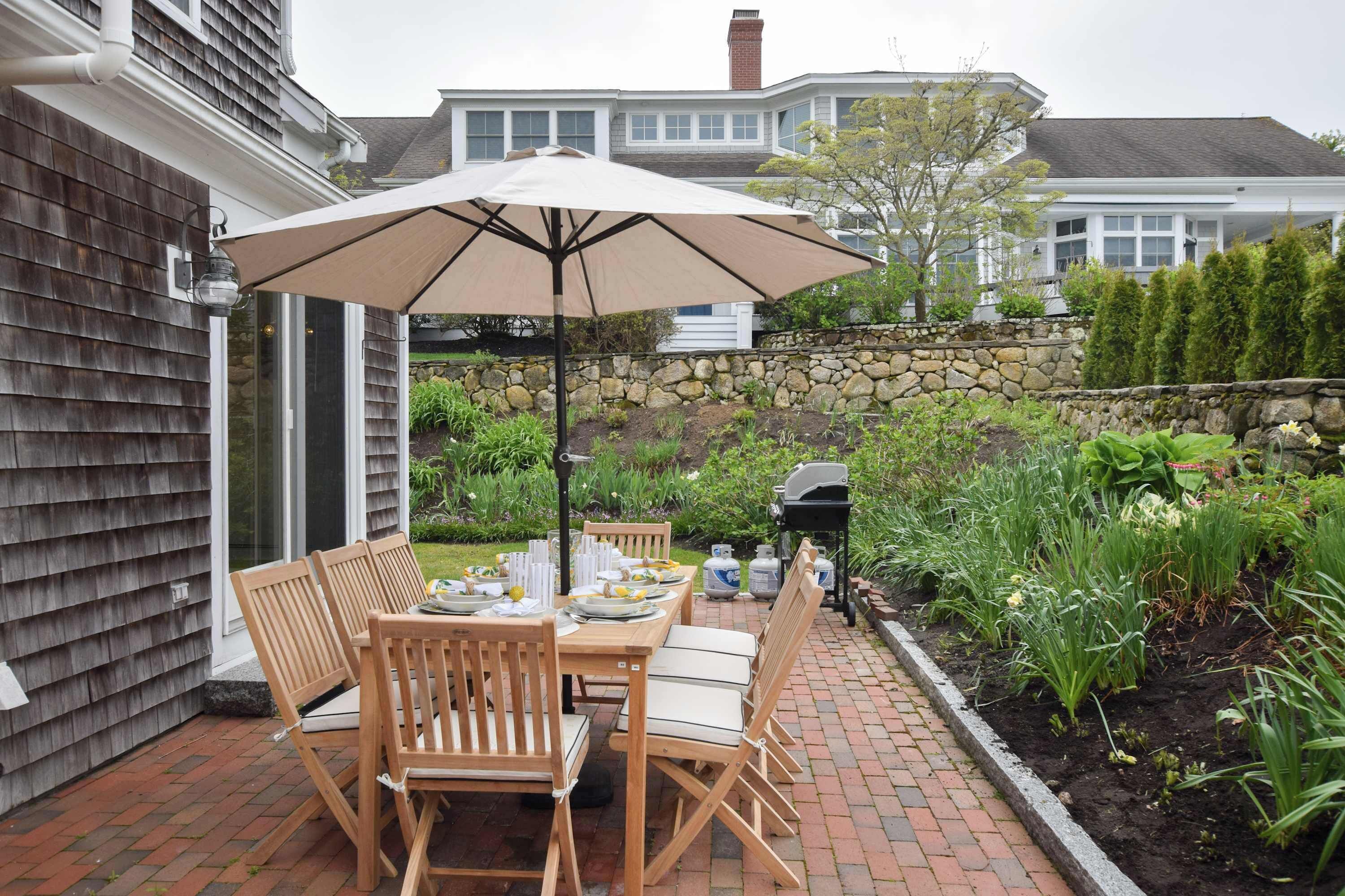 A patio with a table set for dining, surrounded by chairs, and a large umbrella providing shade.
