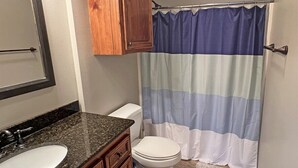 Un baño con un inodoro blanco, un lavamanos con encimera de granito, armarios de madera y una cortina de ducha a rayas.