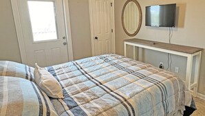Un dormitorio con cama, televisor sobre un mueble, una puerta y una ventana.