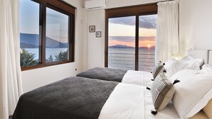 Un dormitorio con dos camas, ventanas amplias con cortinas, vistas al atardecer y una lámpara en el techo.
