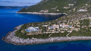 Vista aérea de una propiedad costera con varias edificaciones, un litoral rocoso y un mar azul cristalino.
