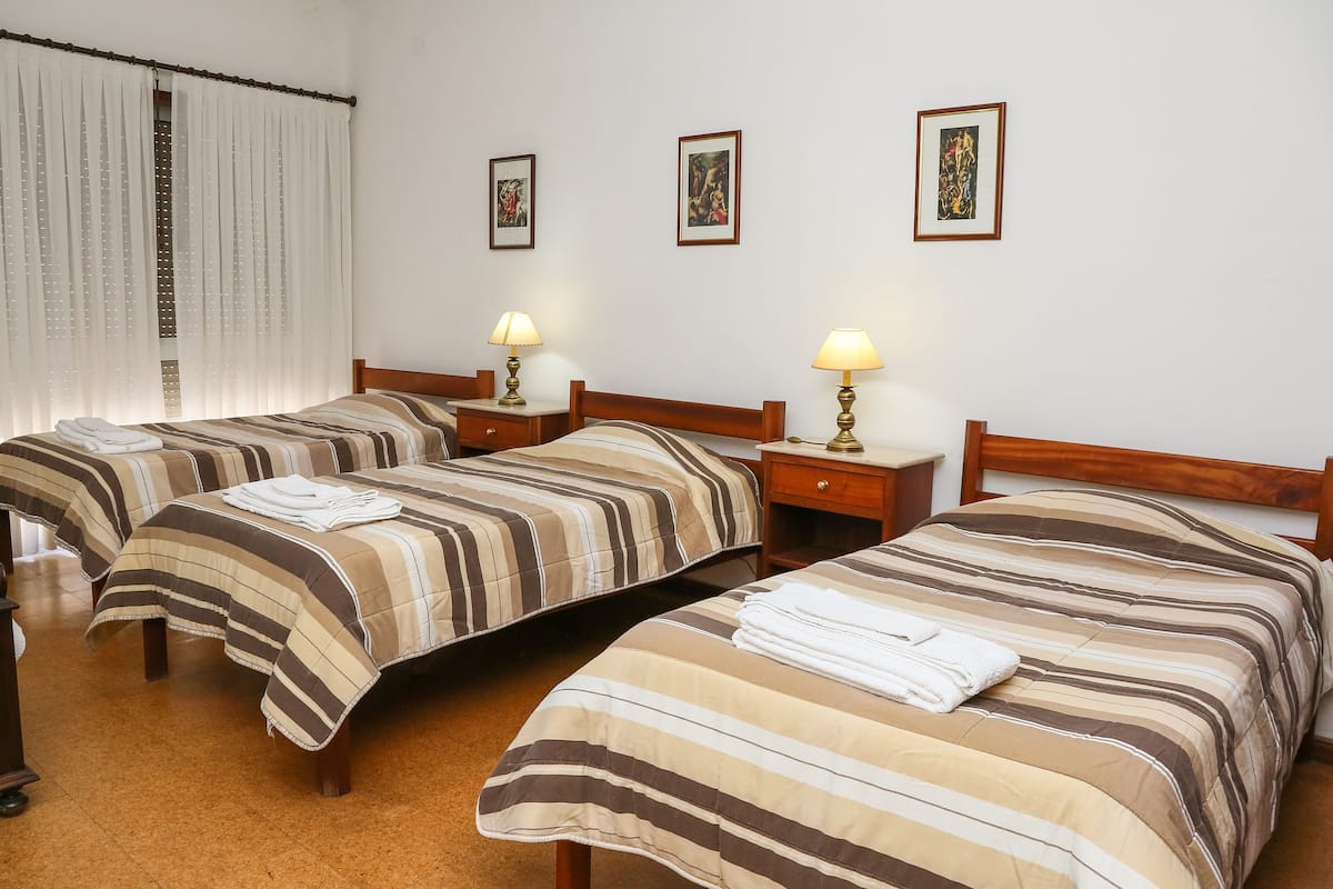 A hotel room with two single beds, each with a striped bedspread and a bedside table with a lamp. There are three framed pictures on the wall.