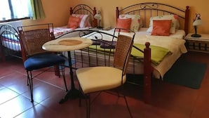 A room with two beds, a dining table with chairs, and a window with curtains. - Penzion Albatros (Cesky Krumlov)