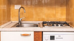 Een keuken met witte kastjes, een roestvrijstalen spoelbak en een gasfornuis.