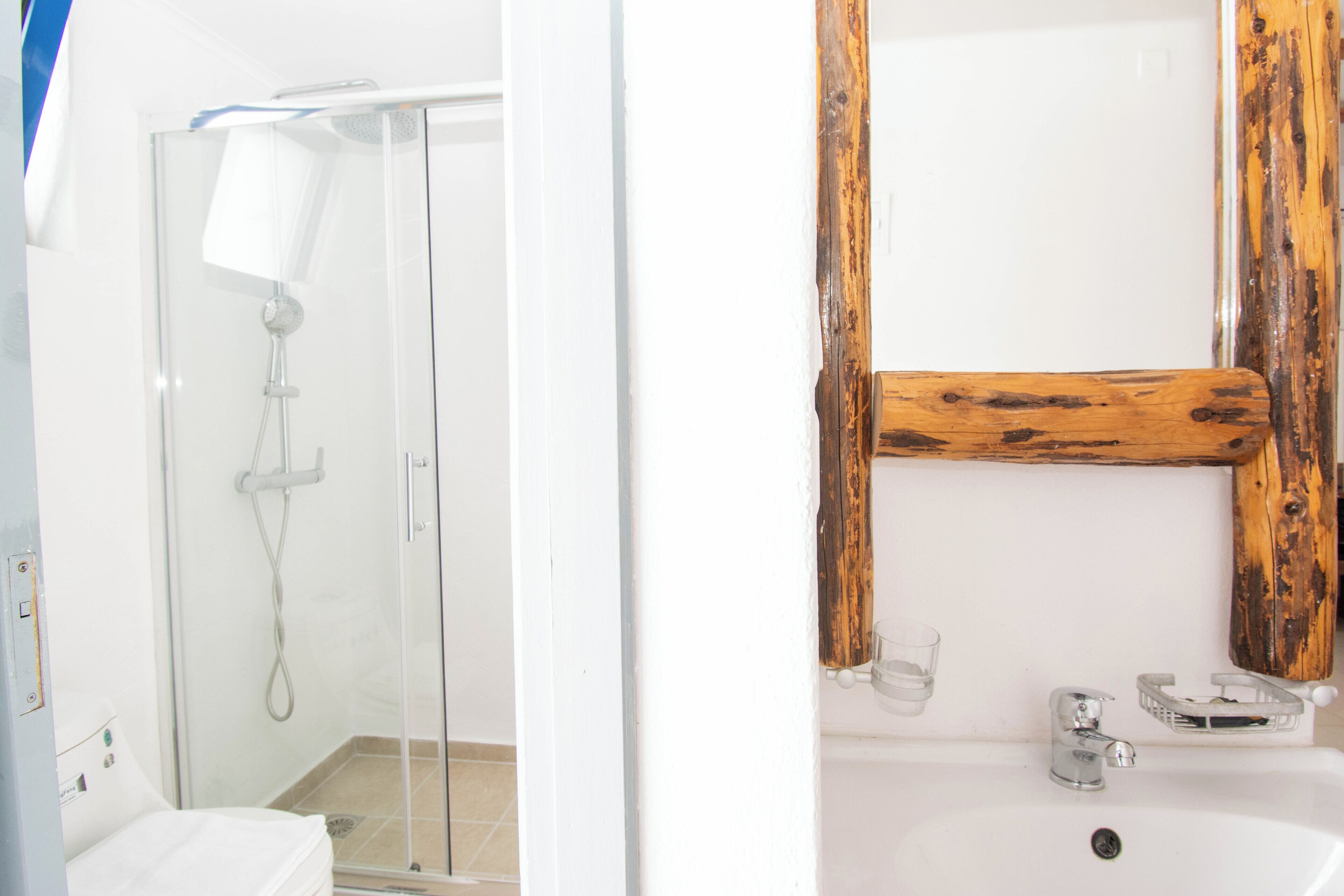 A bathroom with a glass shower enclosure, a wooden-framed mirror, and a sink with a soap dish.