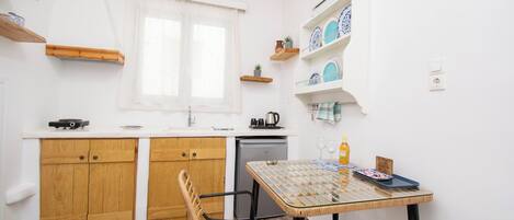 Una cucina compatta con mobili in legno, un piccolo tavolo da pranzo e una finestra con tende leggere.