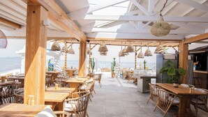 An outdoor restaurant with wooden tables and chairs, hanging lights, and a view of the ocean. - Ov Suites (Hersonissos)