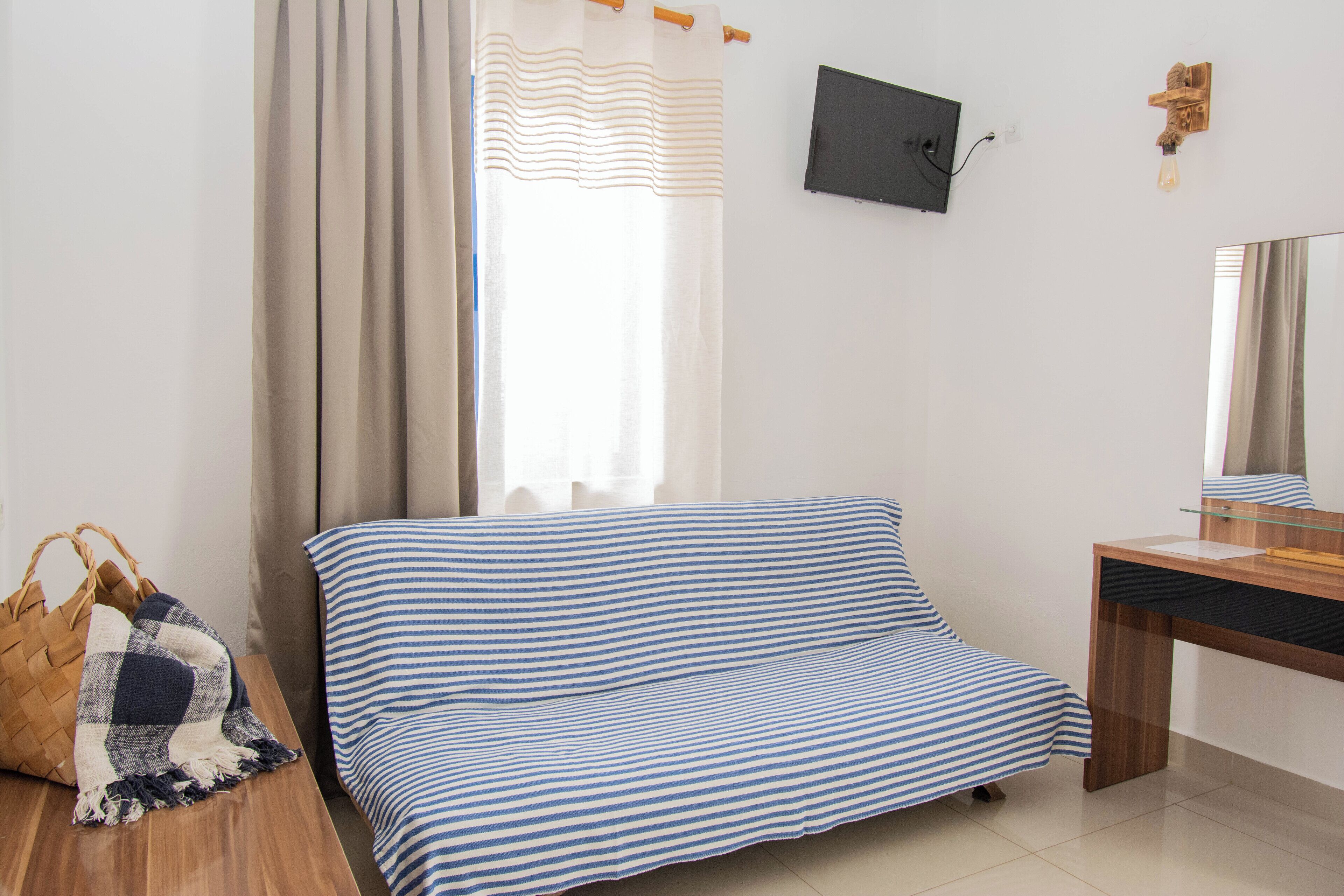 A bedroom with a bed, a wooden desk, a television, and a wall-mounted light fixture.
