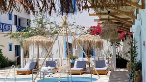 A pool area with lounge chairs and umbrellas, surrounded by stone walls and potted plants. - Ov Suites (Hersonissos)
