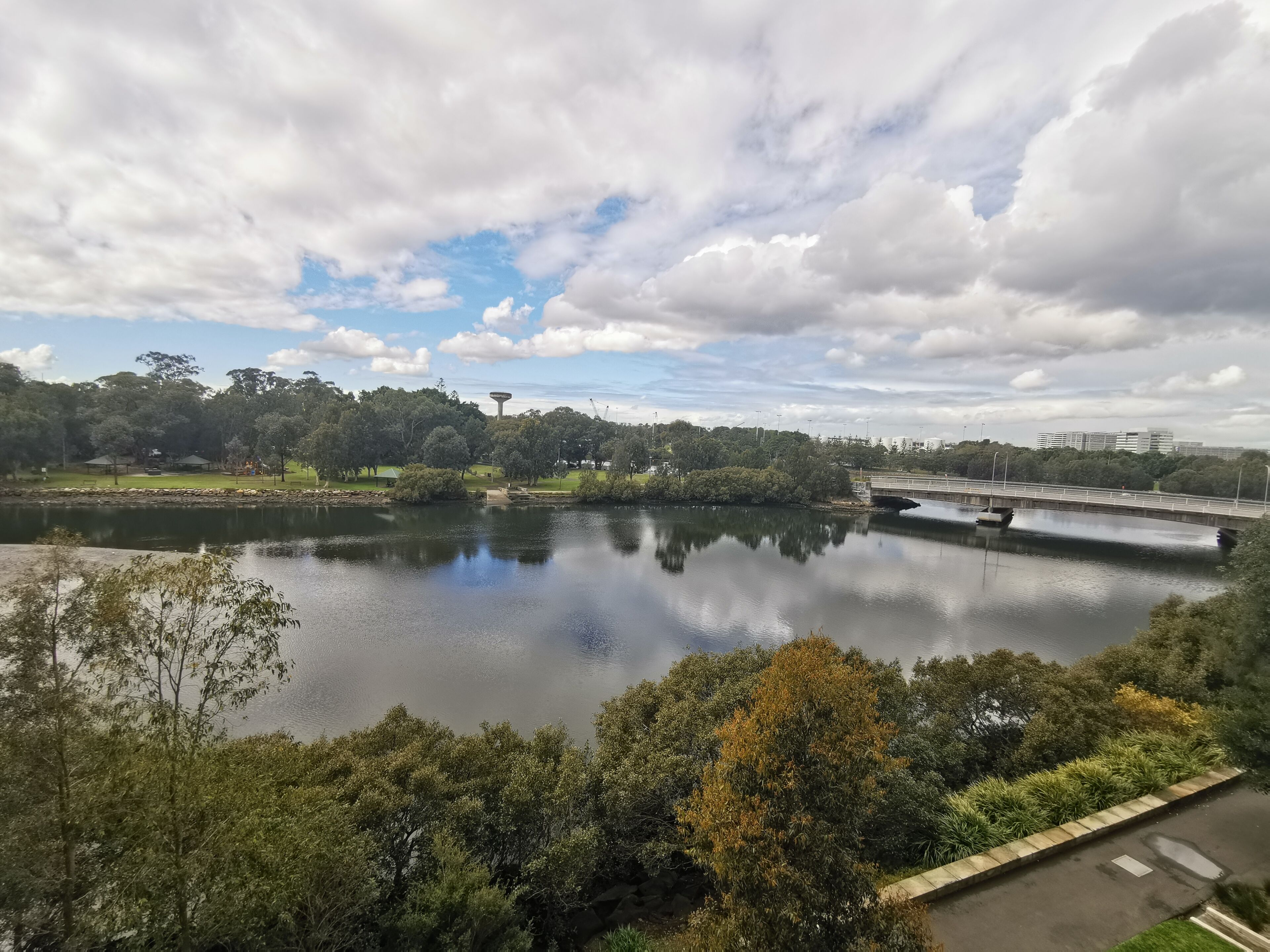 A calm river with a bridge, surrounded by lush greenery and trees.