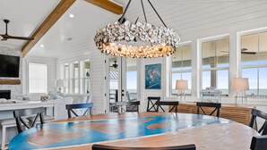 A spacious dining area with a large wooden table, white paneled walls, and a unique shell chandelier.