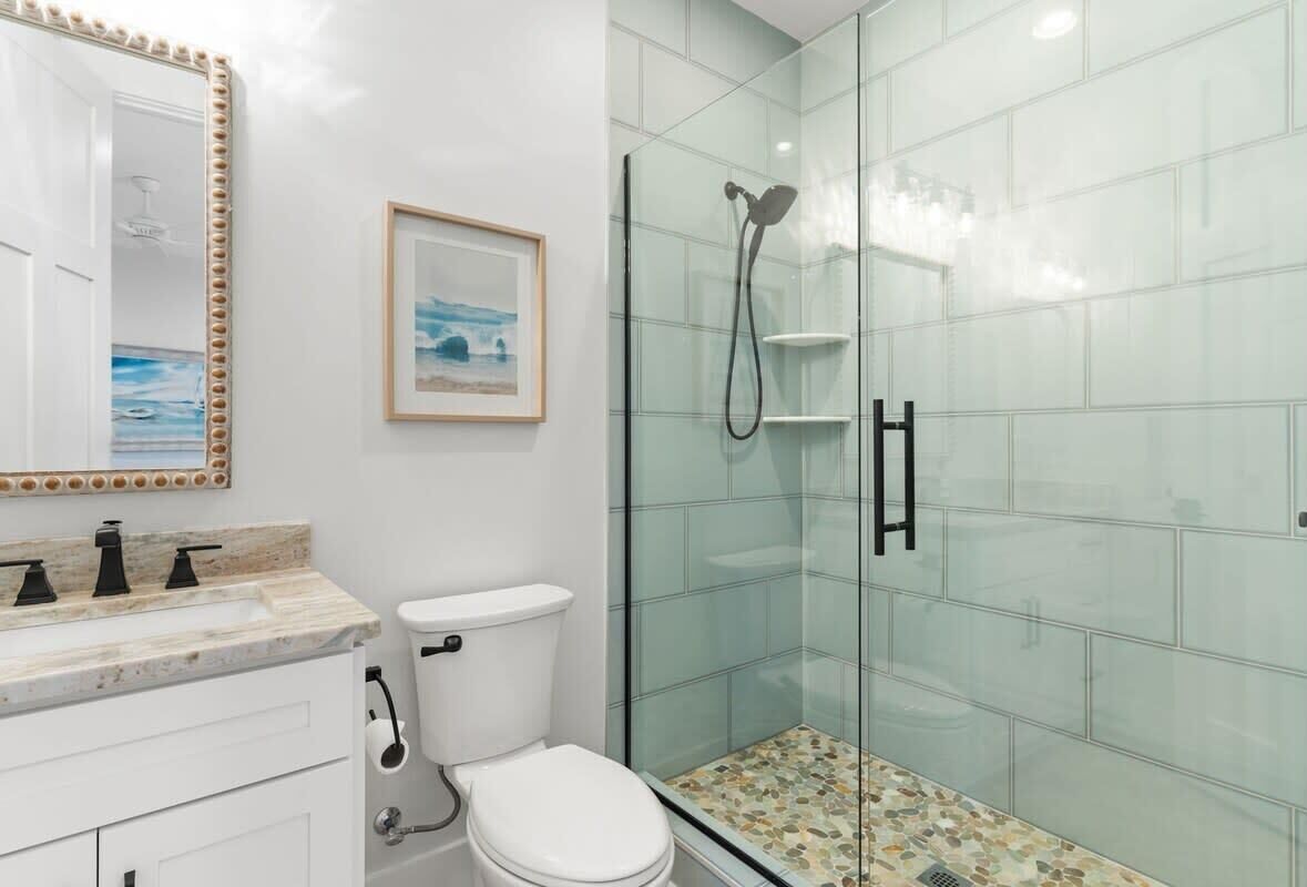 Une salle de bain dotée d’une douche à parois de verre, de toilettes blanches et d’un meuble-lavabo avec un plan de travail en marbre.
