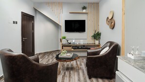 A modern living room with a flat-screen TV, two leather armchairs, a coffee table, and a wooden staircase. - Kashco Apartment Wuse II (Abuja)