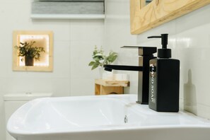 A bathroom with a white sink, a black soap dispenser, and a wooden-framed mirror. - Kashco Apartment Wuse II (Abuja)