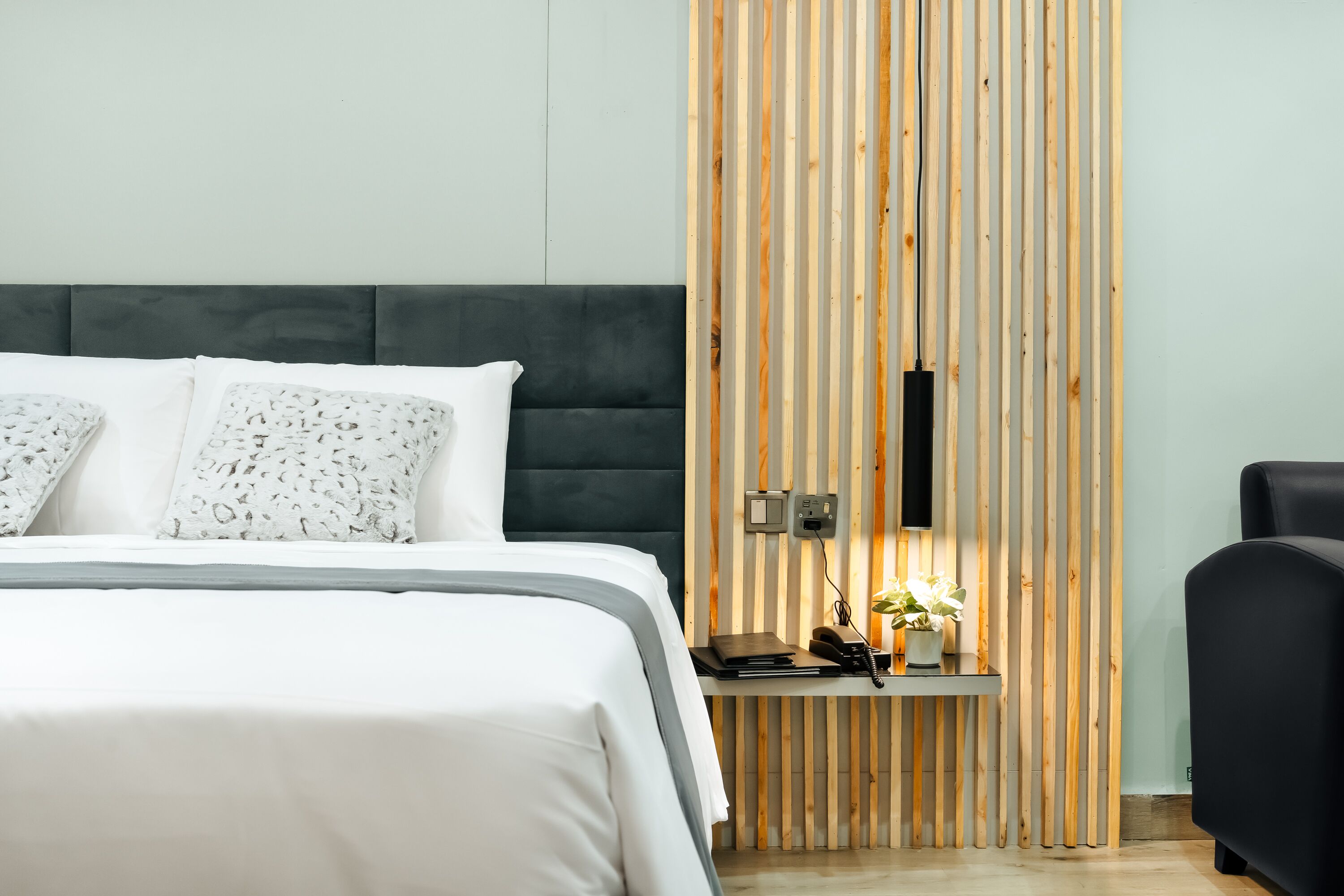 A modern bedroom with a bed, bedside table, and a wooden panel wall.